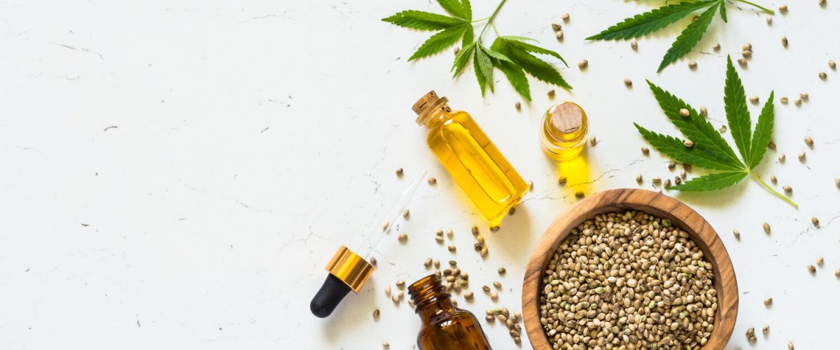 Cannabis oil hemp oil with cannabis seeds and cannabis leaves at white table. Top view with copy space.