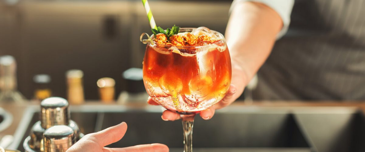 Closeup of alcohol cocktail in cafe. Woman serving beverage in glass with ice cubes and decoration. Small business and professional barman concept