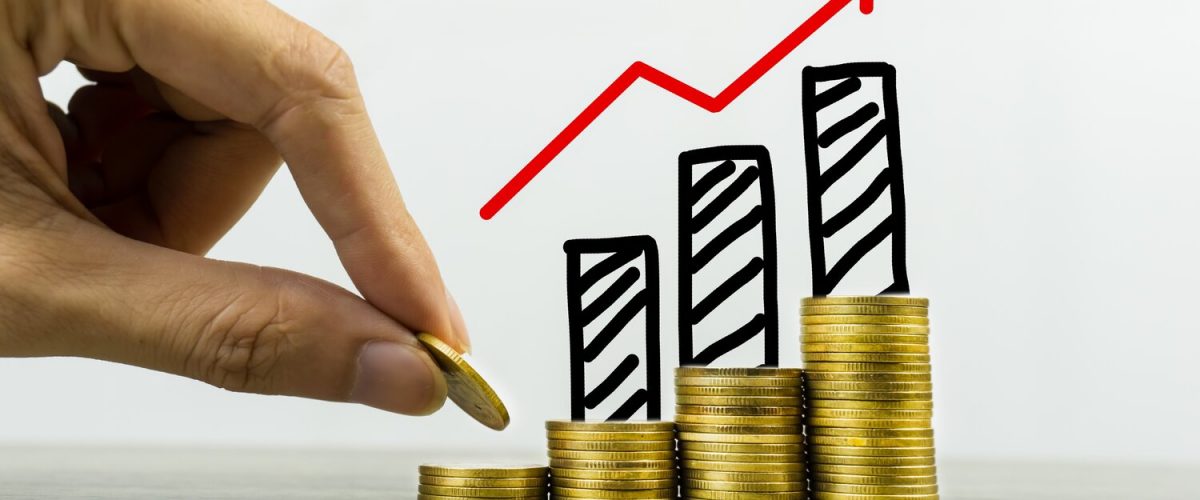 Long-term investment or making money with the right concepts. A business man putting coin on stack of coins on a table with growing graph on coins pile. Depicts a standing and stable investment.