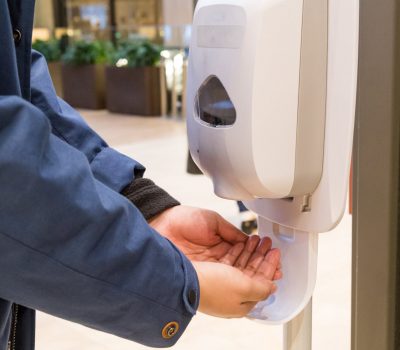 Person cleaning hand with anti-bacterial hand disinfectant sanitizer dispenser in public mall in Japan