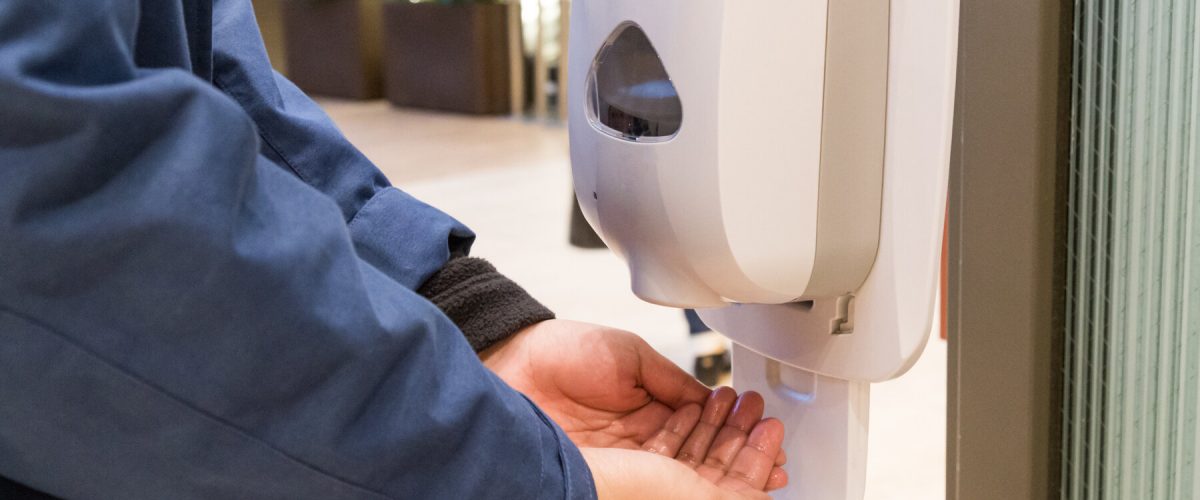 Person cleaning hand with anti-bacterial hand disinfectant sanitizer dispenser in public mall in Japan