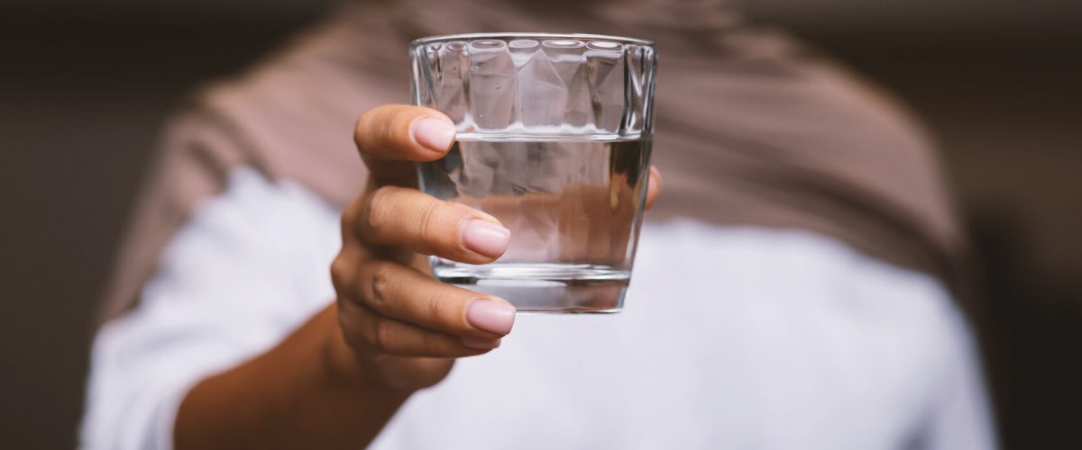Unrecognizable Muslim Woman Offering Glass Of Water To Camera Standing In Modern Kitchen At Home, Wearing Hijab. Healthy Hydration, Drink More Water And Stay Hydrated. Selective Focus, Cropped