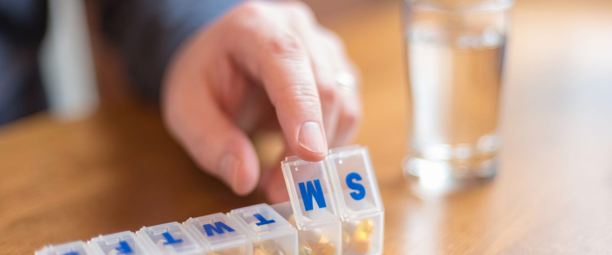 Close up of man's hand using a pill holder to organize daily vitamins and supplements