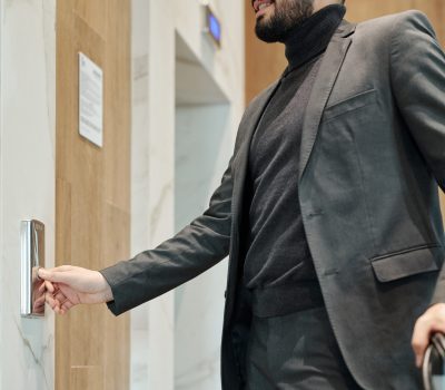 Young elegant businessman pushing button on the wall while standing by door and waiting for elevator in hotel
