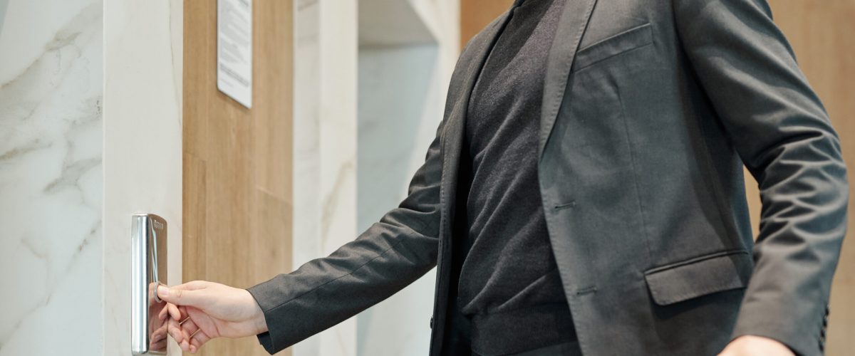 Young elegant businessman pushing button on the wall while standing by door and waiting for elevator in hotel